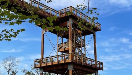 A wooden observation tower surrounded by trees under a blue sky with scattered clouds.