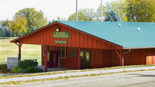 A red building with a green roof, labeled "R. Badger Mining Museum," set in a grassy area with trees in the background.