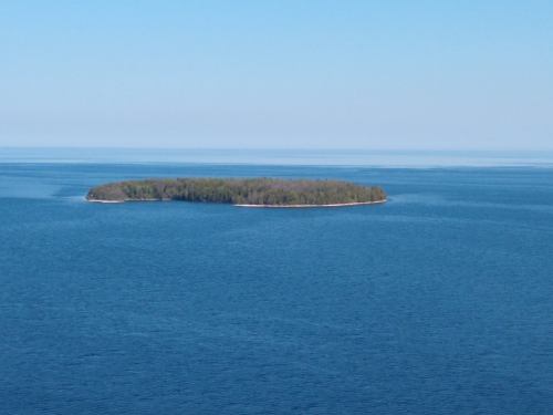 A small, wooded island surrounded by calm blue waters under a clear sky.