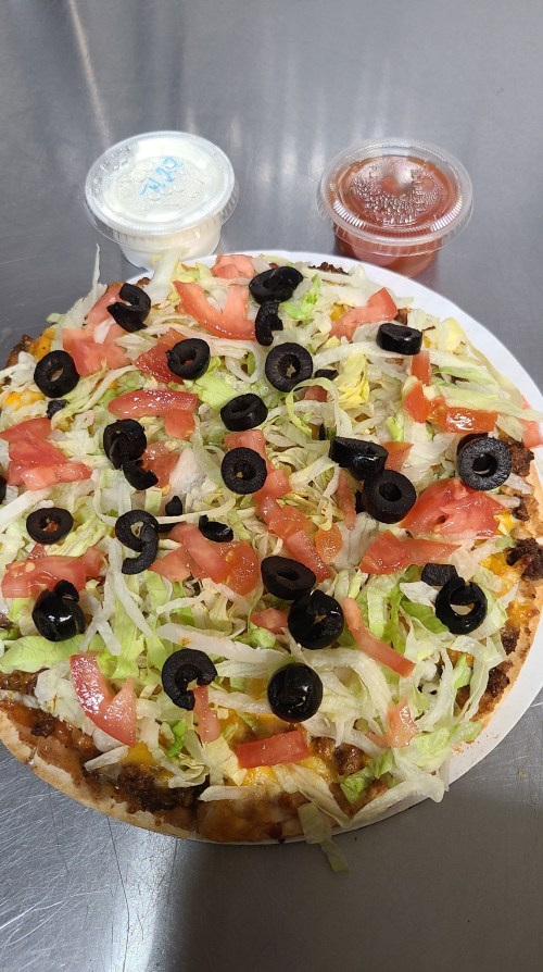A pizza topped with lettuce, tomatoes, black olives, and served with two dipping sauces.