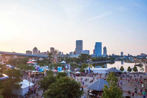 A vibrant city skyline at sunset, with a bustling park, a ferris wheel, and crowds enjoying the outdoor festivities.