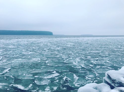 A serene winter landscape featuring a frozen lake with ice patches and a misty horizon under a cloudy sky.