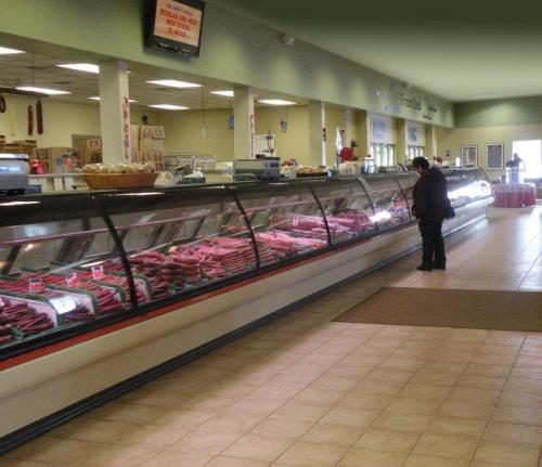 A shopper examines a display of various meats in a well-lit grocery store.