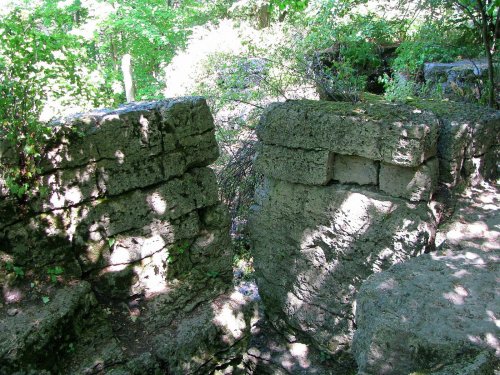 Two weathered stone structures surrounded by lush greenery and dappled sunlight in a natural setting.