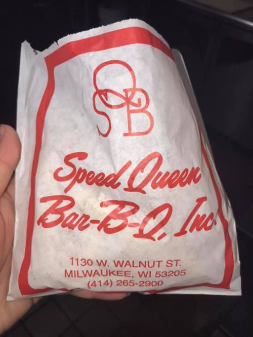 A hand holding a takeout bag from Speed Queen Bar-B-Q, featuring the restaurant's logo and address in Milwaukee, WI.