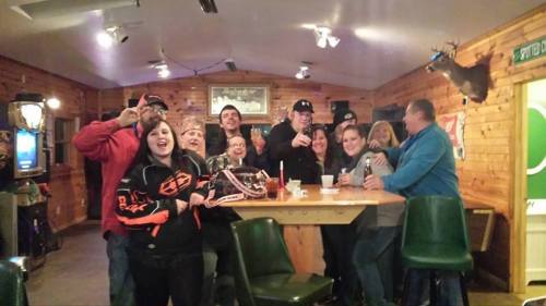 A group of people smiling and posing together at a bar with wooden walls and a table.