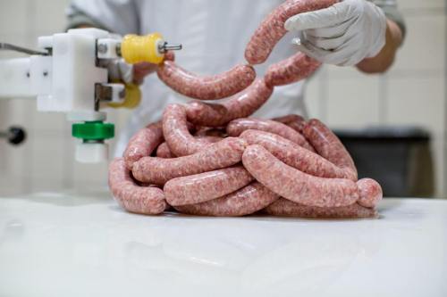 A person in gloves holds freshly made sausages, with more sausages piled on a white surface.