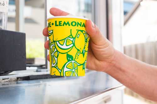 A hand holding a colorful cup decorated with lemons and bananas, filled with a refreshing drink.