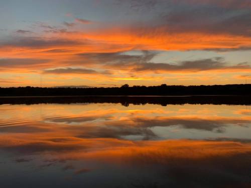 A serene sunset over a calm lake, with vibrant orange and pink clouds reflected in the water.