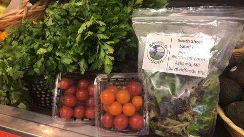 Fresh produce display featuring cilantro, cherry tomatoes, and a salad mix from Bayfield Foods.