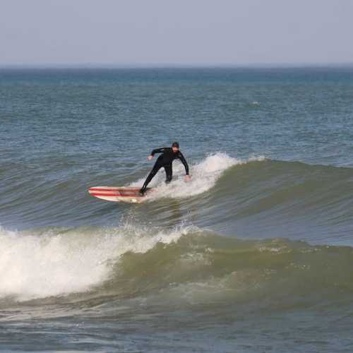 A surfer in a black wetsuit rides a wave on a red surfboard against a blue ocean backdrop.