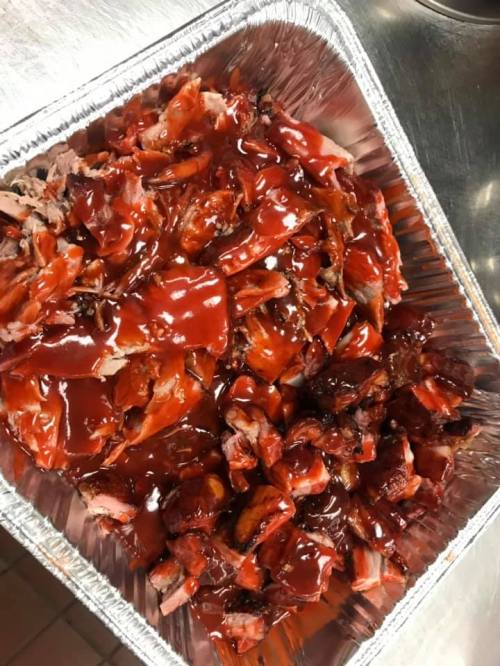 A tray filled with shredded barbecue meat covered in a rich red barbecue sauce.