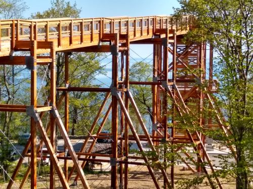 A wooden observation tower with a walkway, surrounded by trees and overlooking a scenic view.