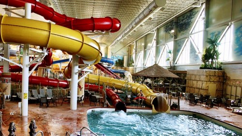 Indoor water park featuring colorful water slides, a pool, and lounge chairs in a bright, spacious environment.