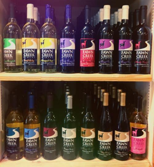 A display of various Fawn Creek wine bottles arranged on wooden shelves.
