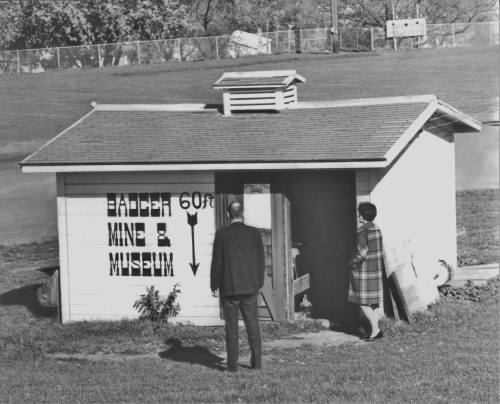 A man and woman stand outside a small building labeled "Badger Mine & Museum," with an arrow pointing down.