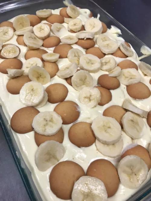A glass dish filled with layered banana pudding, topped with sliced bananas and vanilla wafers.