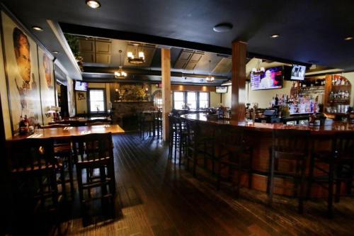 Interior of a restaurant with wooden floors, bar area, and tables, featuring warm lighting and a cozy atmosphere.