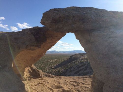 A natural rock arch frames a scenic view of desert landscape and distant mountains under a blue sky.