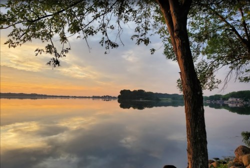 A serene lake at sunset, reflecting trees and clouds, with calm waters and a peaceful atmosphere.