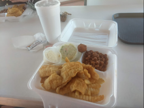 A takeout container with crinkle-cut fries, a small serving of coleslaw, and a side of baked beans. A drink is nearby.