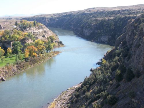 A serene river winding through rocky cliffs and lush greenery under a clear blue sky.