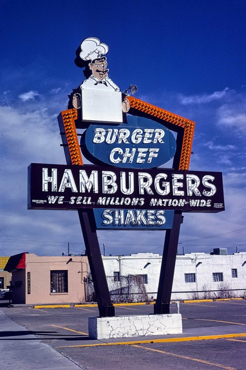 Vintage Burger Chef sign featuring a chef, advertising hamburgers and shakes against a blue sky.