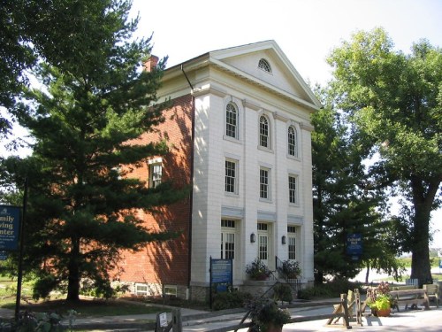 Historic building with a mix of brick and white facade, surrounded by trees and signage for a family history center.