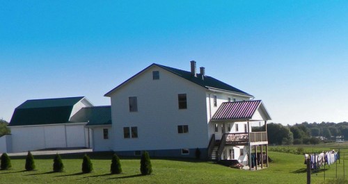 A large white house with a green roof, surrounded by a grassy field and a clothesline in the foreground.