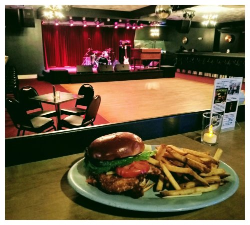 A plate with a burger and fries in front of a stage with musical instruments and dim lighting.