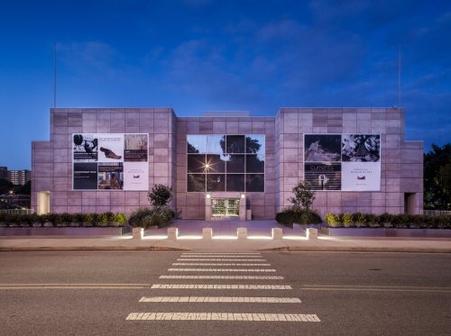 Modern art museum exterior at dusk, featuring large promotional banners and illuminated landscaping.