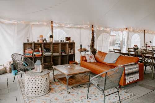 Cozy tent interior with an orange sofa, wooden shelves, a round table, and string lights, creating a warm atmosphere.