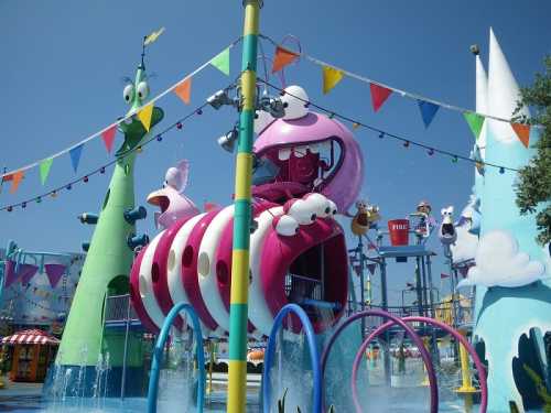 Colorful water play area with slides, fountains, and whimsical characters under a clear blue sky.