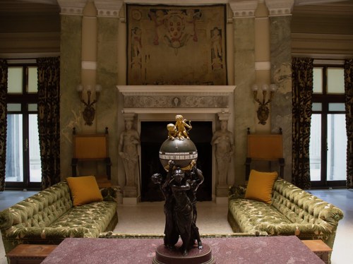 Elegant room featuring a globe statue, ornate decor, green sofas, and a large tapestry on the wall.