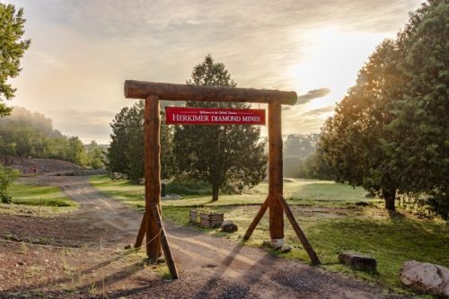Sign at the entrance of Herkimer Diamond Mines, surrounded by trees and a scenic landscape at sunrise.