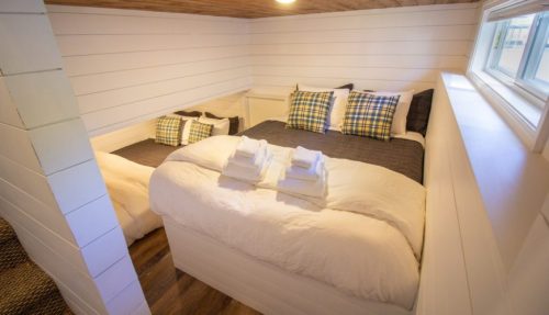 Cozy bedroom with two beds, white walls, wooden ceiling, and neatly arranged pillows and towels.