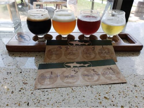 Four small glasses of beer in a wooden flight holder, with a tasting card showing names and ratings.