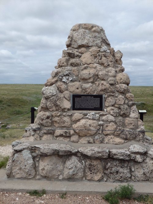 A stone monument with a plaque, set against a grassy landscape under a cloudy sky.