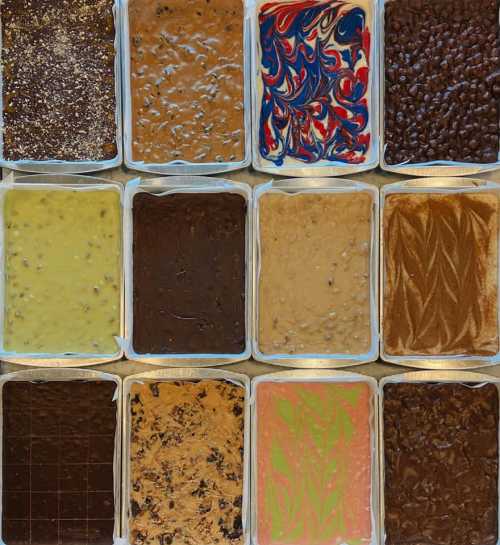 A grid of colorful, textured desserts in various flavors and patterns, arranged in twelve rectangular containers.