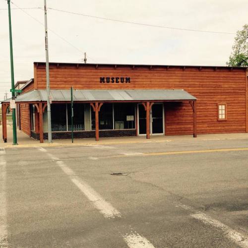 A wooden building with a sign reading "MUSEUM," located on a street with power lines and trees in the background.