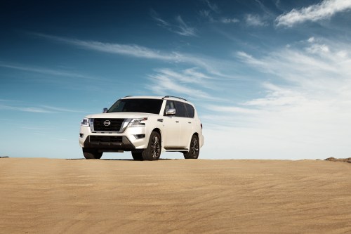 A white Nissan SUV parked on a sandy landscape under a clear blue sky.