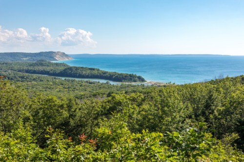 A scenic view of lush green hills meeting a tranquil blue lake under a clear sky.