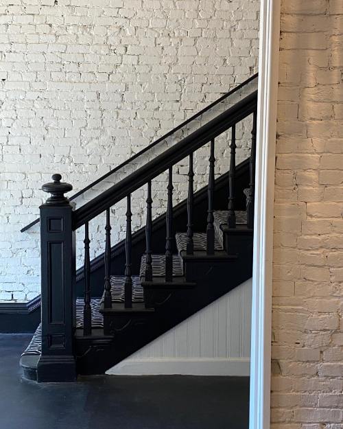 A black staircase with decorative railings against a white brick wall.