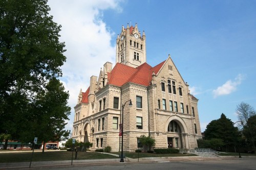 Historic stone building with a clock tower, surrounded by trees and a blue sky.