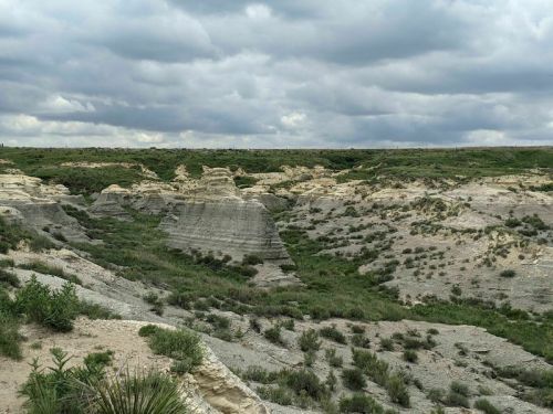 A rugged landscape with layered rock formations and sparse vegetation under a cloudy sky.
