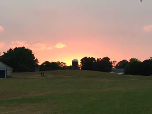 A serene landscape at sunset, featuring a silhouette of a barn and a silo against a colorful sky.