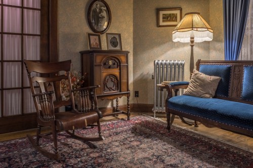 Cozy vintage living room with a rocking chair, blue sofa, lamp, and decorative items on the walls and furniture.
