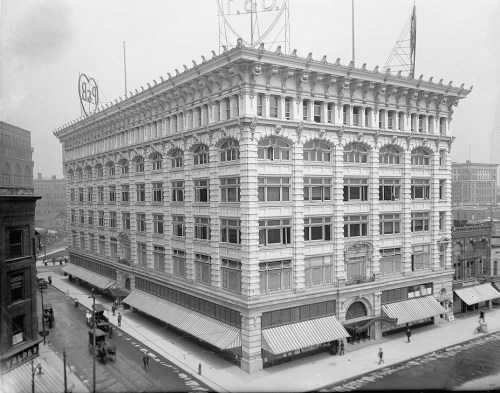 Historic black-and-white photo of a grand, ornate building with large windows and decorative architecture.