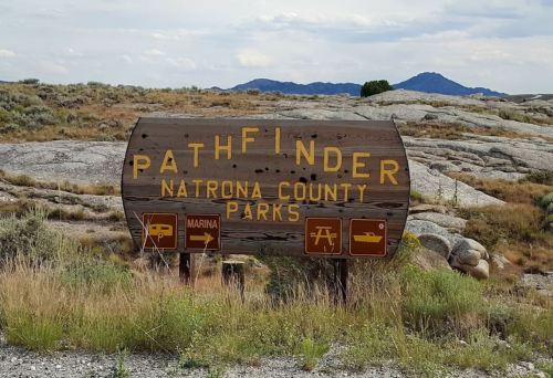 Wooden sign for Pathfinder Natrona County Parks, featuring icons for a marina and picnic area, set against a rocky landscape.
