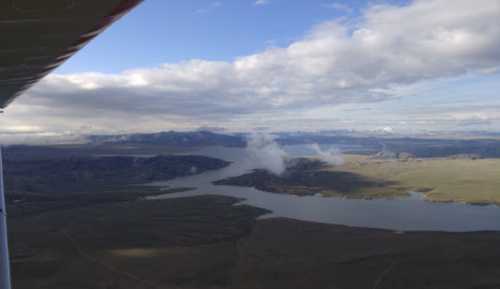 Aerial view of a vast landscape with a river, mountains, and clouds under a blue sky.